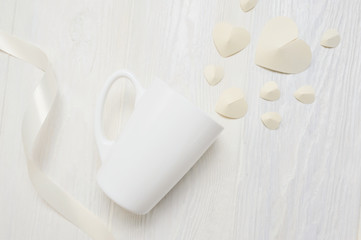 Mockup for St. Valentine's Day greeting card. mug and white paper heart flatlay on a white wooden background, with place for your text. Flat lay, top view photo mock up
