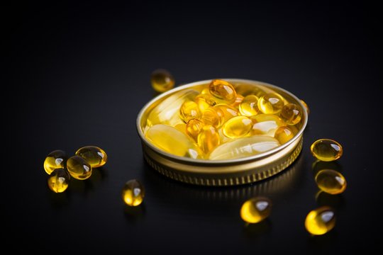 Capsules Of Fish Oil In Gold Cup On Black Background