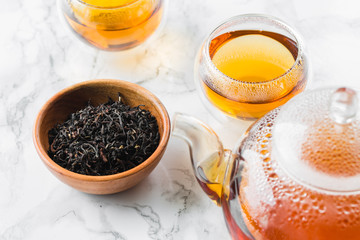 Dry tea in wooden plate and glass cup of tea on marble background