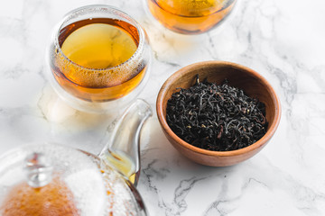 Dry tea in wooden plate and glass cup of tea on marble background