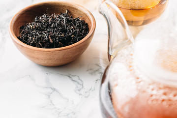 Dry tea in wooden plate and glass cup of tea on marble background