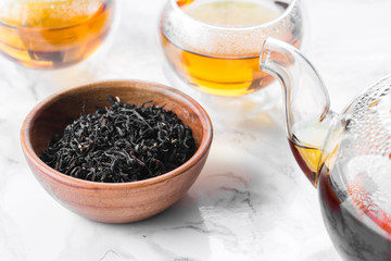 Dry tea in wooden plate and glass cup of tea on marble background
