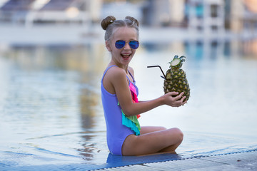 Child drinking juice in swimming pool bar. Summer family vacation with kids. Little girl holding fresh pineapple cocktail in swim up beach cafe. Kid with tropical fruit lemonade in luxury resort.