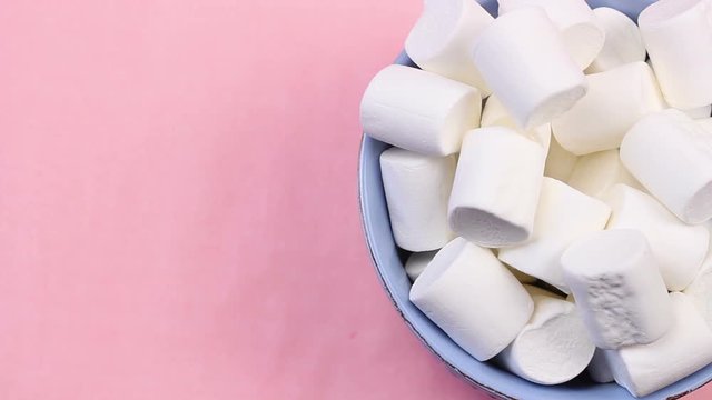 Marshmallows in blue plate on pastel pink background.