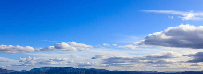 Obraz na płótnie Canvas Blue sky background with scattered clouds over mountains silhouette. Aerial, panoramic photo banner