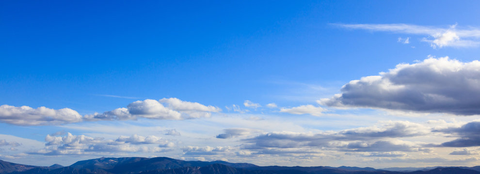 Blue sky background with scattered clouds over mountains silhouette. Aerial, panoramic photo banner