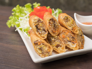 Fried spring rolls with sweet, sour and spicy sauces, served with fresh vegetable on wooden table with copy space. Asian food.