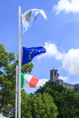 Flags of San Marino, European Union, Italy against the background of a medieval  historical castle of San Marino.