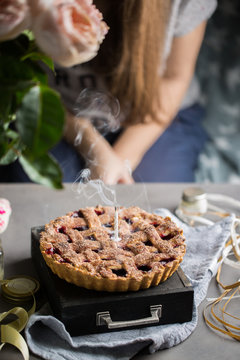 A birthday cherry cake with a burning one white candle. Atmospheric beautiful food birthday photo with home cherry pie, flowers, ribbons and decoration.