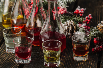 Assorted alcoholic cordials in glasses and decanters with Christmas decorations on dark wood background
