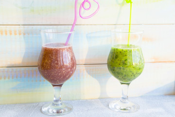 Fresh Fitness Smoothie Concept. Glasses of green and purple fruit and berry smoothie against a light colored wooden wall
