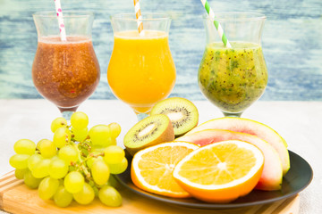 Tropical Healthy Smoothie and a plate of fresh fruit: kiwi, orange, watermelon and grape on a light table against a blue wooden wall. Diet, Detox, Healthy Dessert Concept
