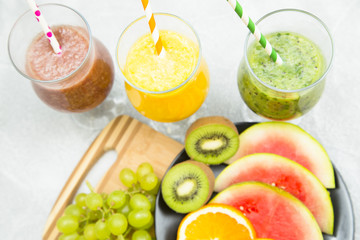 Tropical Healthy Smoothie and a plate of fresh fruit: kiwi, orange, watermelon and grape on a light table against a blue wooden wall, top view. Diet, Detox, Healthy Dessert Concept