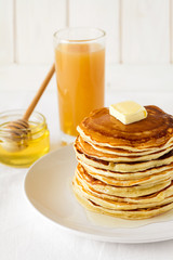 Stack of pancakes with butter and honey on white background