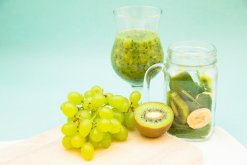 Preparing green smoothie with kiwi, banana, grapes and spinach on a wooden cutting board, light blue background. Diet, Fitness, Dessert Concept