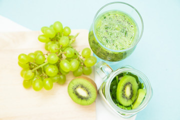 Preparing green smoothie with kiwi, banana, grapes and spinach on a wooden cutting board, light blue background, top view Diet, Fitness, Dessert Concept