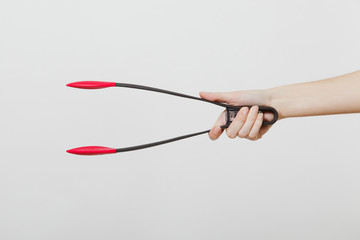 Close up of female hand horizontal holding black and red kitchen salat serving plastic pair of tongs isolated on white background. Kitchen utensils concept. Copy space for advertisement.