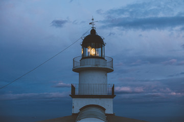 Fototapeta na wymiar Minimalistic and geometrical symmetry shot of beautiful vintage lighthouse on top of cliff, shines light into ocean on amazing and inspiring sunset night, with purple and pink skies