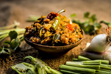 Close up of Indian Dish eaten in winter season Baingan ka Bharta with vegetables like:Spring onions,Allium fistulosum,Coriander,Coriandrum sativum,Garlic,Allium sativum and chills. - obrazy, fototapety, plakaty