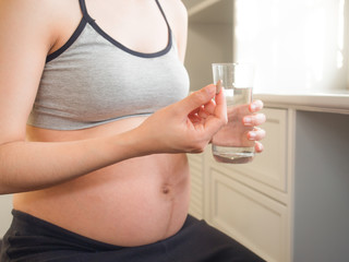 Healthcare, treatment, supplements. pregnant woman holding vitamins with a glass of water.