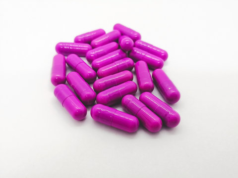 Medication and healthcare concept. Many purple capsules of Clindamycin 300 mg. isolated on white background, used to treat serious infections caused by bacteria. Focus on foreground and copy space.