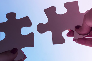 Obraz premium two hands trying to connect couple puzzle piece on sky background. one part of whole. symbol of association and connection. business strategy.