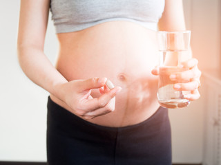 Healthcare, treatment, supplements. pregnant woman holding vitamins with a glass of water.