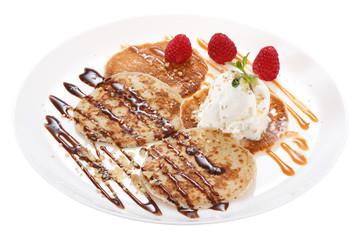 Serving pancakes with ice cream on the plate. Decorated with chocolate syrup, caramel syrup, fresh berries and mint. Isolated on white background.