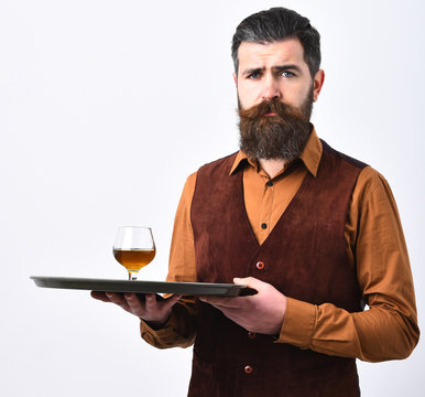 Barman in vintage vest with thoughtful face serves cognac.
