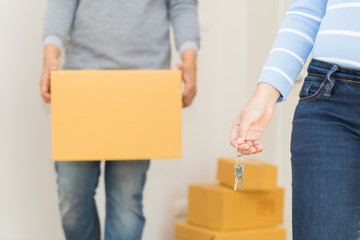 Close up of hand holding a key while a man holding a box to move in - buying new house concept