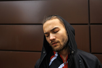 Portrait of a bearded handsome young white guy in the hood posing opposite the futuristic urban...