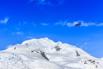 Small red plane flying among clouds over snow peaks and glaciers, Hald Moon island,  Antarctic peninsula