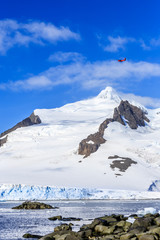 Small red plane flying over snow peaks, glaciers and sea fjord, Hald Moon island,  Antarctic peninsula