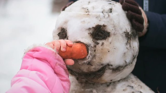 Little girl without gloves inserts carrot snowman instead nose