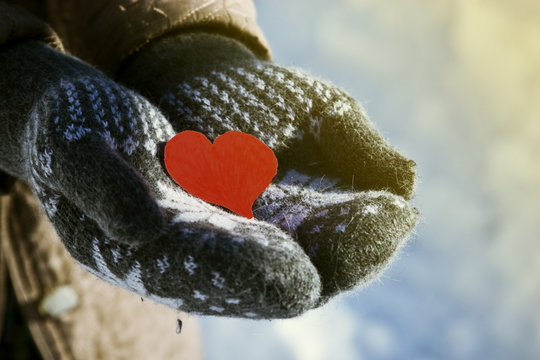 Red heart in the hands of an old grandmother against the background of winter snow close up
