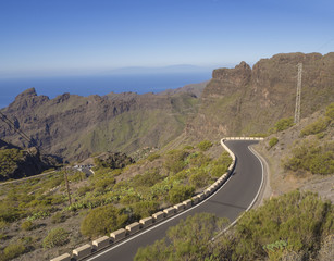 winding asfalt road to village Masca with green hills, sharp mountain peaks, sea horizon and clear blue sky background