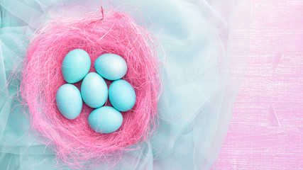 Fototapeta na wymiar Easter eggs in a pink nest. Blue or turquoise chicken eggs on pink wooden background. Pink feather, green plant, flowers