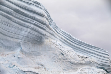 warstwy śniegu i lodu w odłamanym fragmencie góry lodowej z szarym niebem w tle