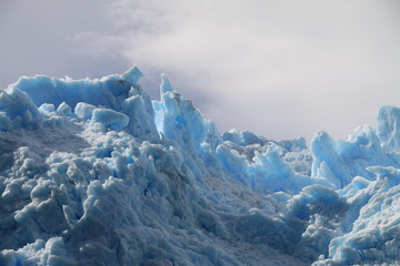 ostre krawędzie czoła lodowca w kolorze biało niebieskim w zbliżeniu z zachmurzonym niebem w tle