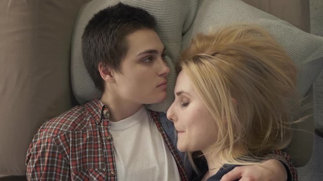 Two young lesbian girls are lying on the bed, a girl with short hair kisses her partner in the forehead, an LGBT family concept, they sleep. 60 fps