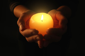 Young woman holding burning candle in darkness