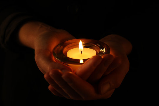 Young woman holding burning candle in darkness