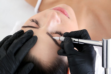 Young woman undergoing procedure of eyebrow permanent makeup in beauty salon, closeup