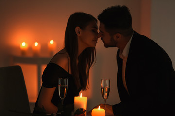 Young couple kissing while sitting at table with burning candles © Africa Studio