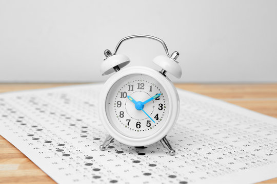 Alarm Clock And Test Sheet On Table, Closeup. Preparation For Exam