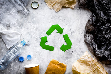 Eco-friendly life. Green paper recycling sign among waste paper, plastic, polyethylene on grey...