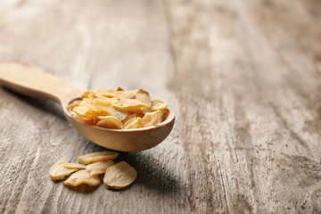 Spoon with dried garlic flakes on wooden background