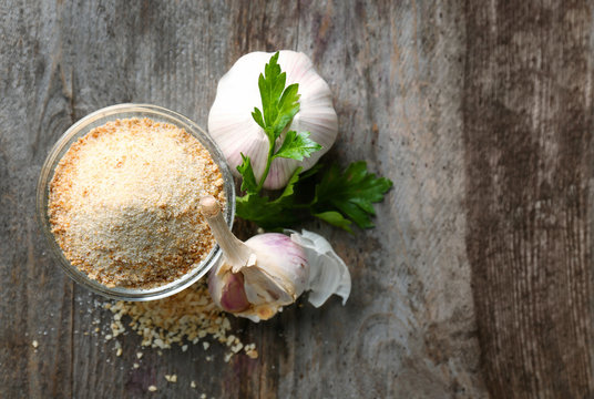 Bowl with dried garlic powder on wooden background