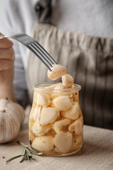 Woman trying preserved garlic on table, closeup