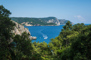 Scenic view on the Ionian sea through the trees. Speedboat sails on the sea.